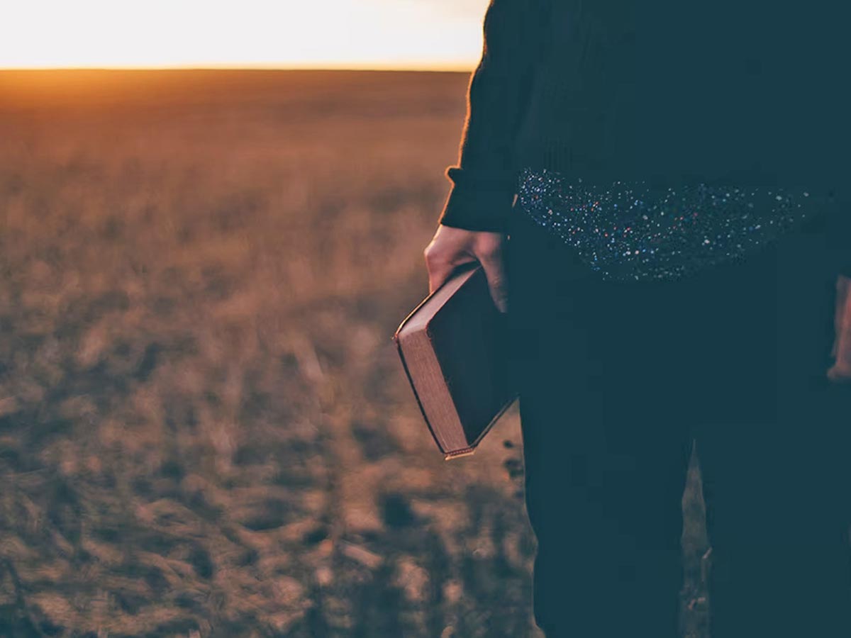 Image of someone walking through a field carrying their bible