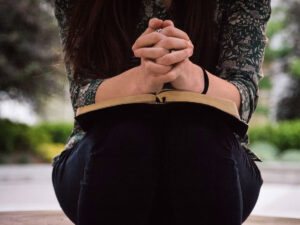 An image of a woman sitting with a bible on her lap and her hands clasped